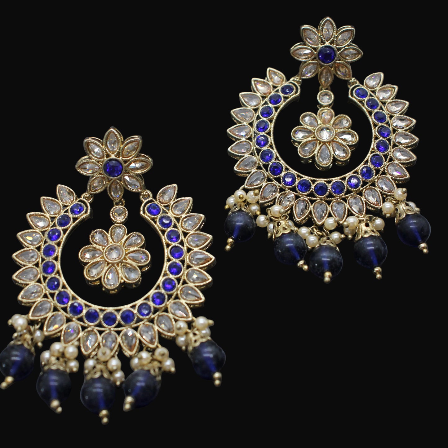 Ornate earrings with blue stones and gold detailing on a dark background