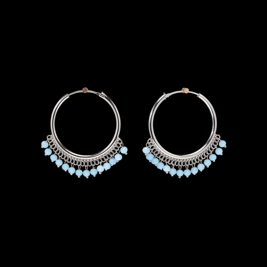 A pair of silver hoop earrings with dangling chains and small light blue beads, displayed on a textured brown background.