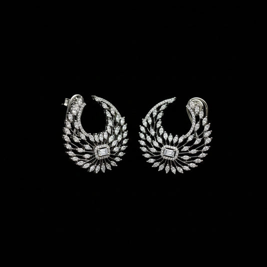 A pair of silver-toned crescent-shaped earrings adorned with numerous clear stones, featuring a central square-cut stone, displayed on a dark gray background.