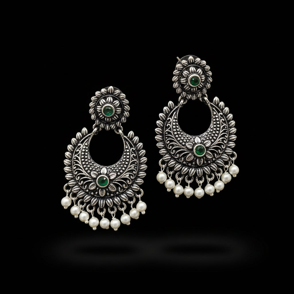 Pair of silver earrings with green stones and pearl-like beads on a gray background, branded 'Saheeli'.