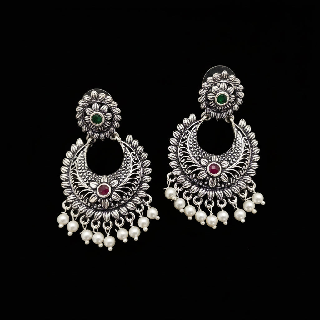 Pair of silver earrings with pearls and gemstones on a gray background, branded 'Saheli'.