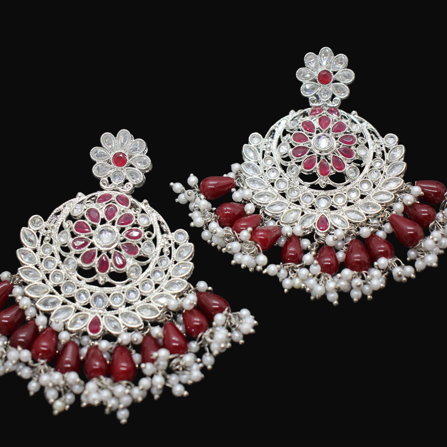 Pair of ornate earrings with red stones and pearl-like elements on a dark background