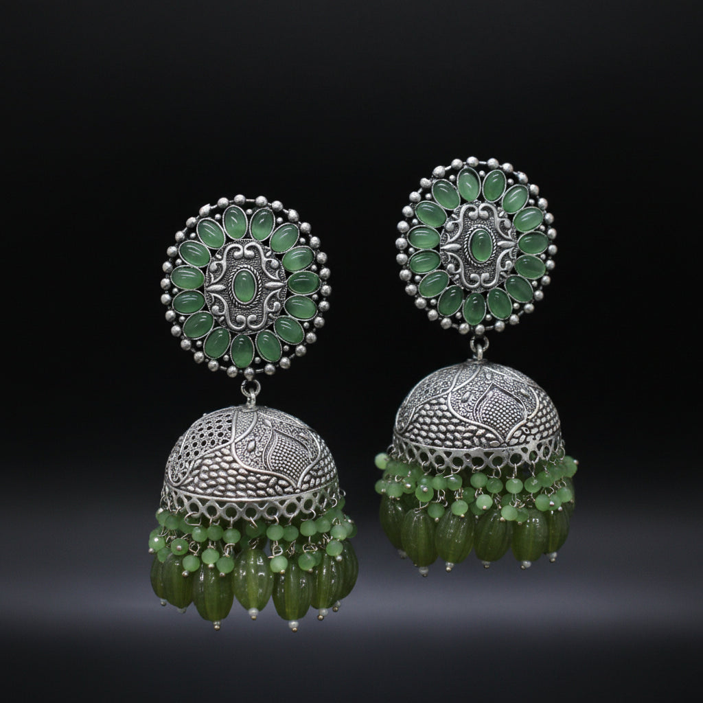 Pair of silver and green jhumka earrings on a black background
