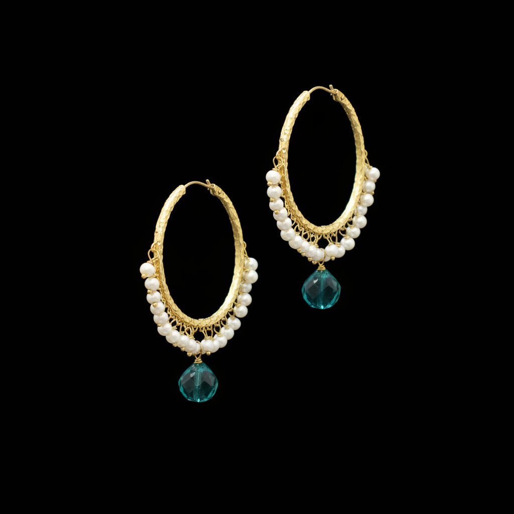 A pair of gold hoop earrings decorated with dangling white pearl-like beads and faceted green teardrop charms, displayed on a dark gray background.