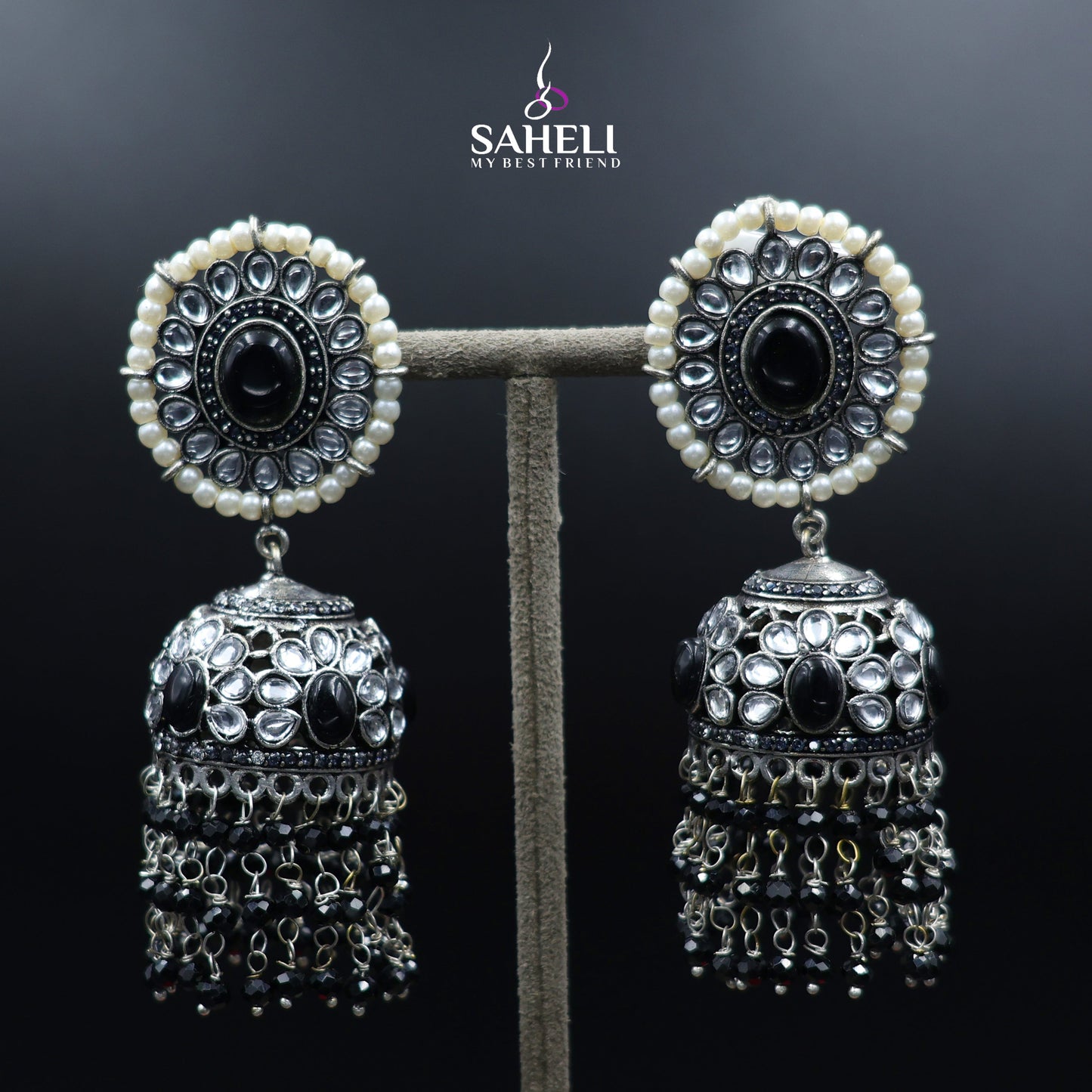 Pair of silver and black earrings on a stand with 'Saheli' branding.