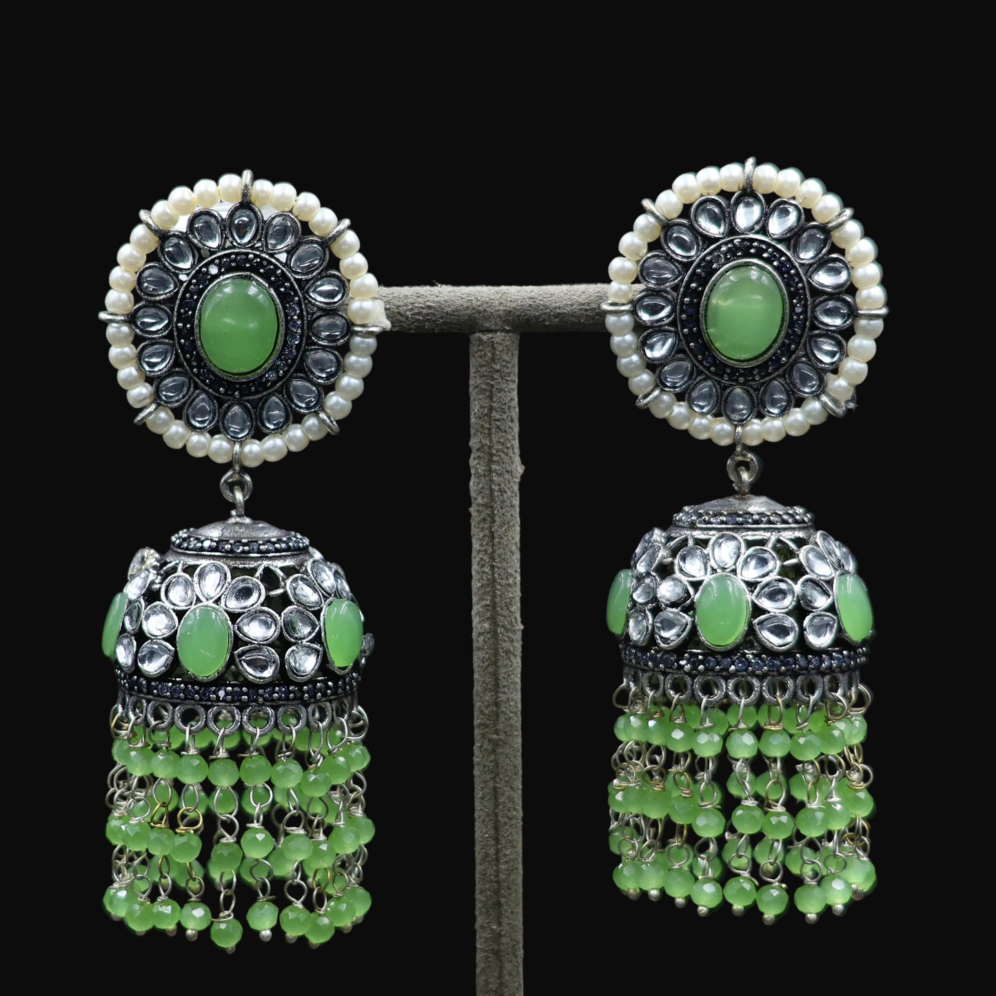 Pair of green gemstone earrings with silver and pearl accents on a dark background, featuring the brand 'Saheli'.