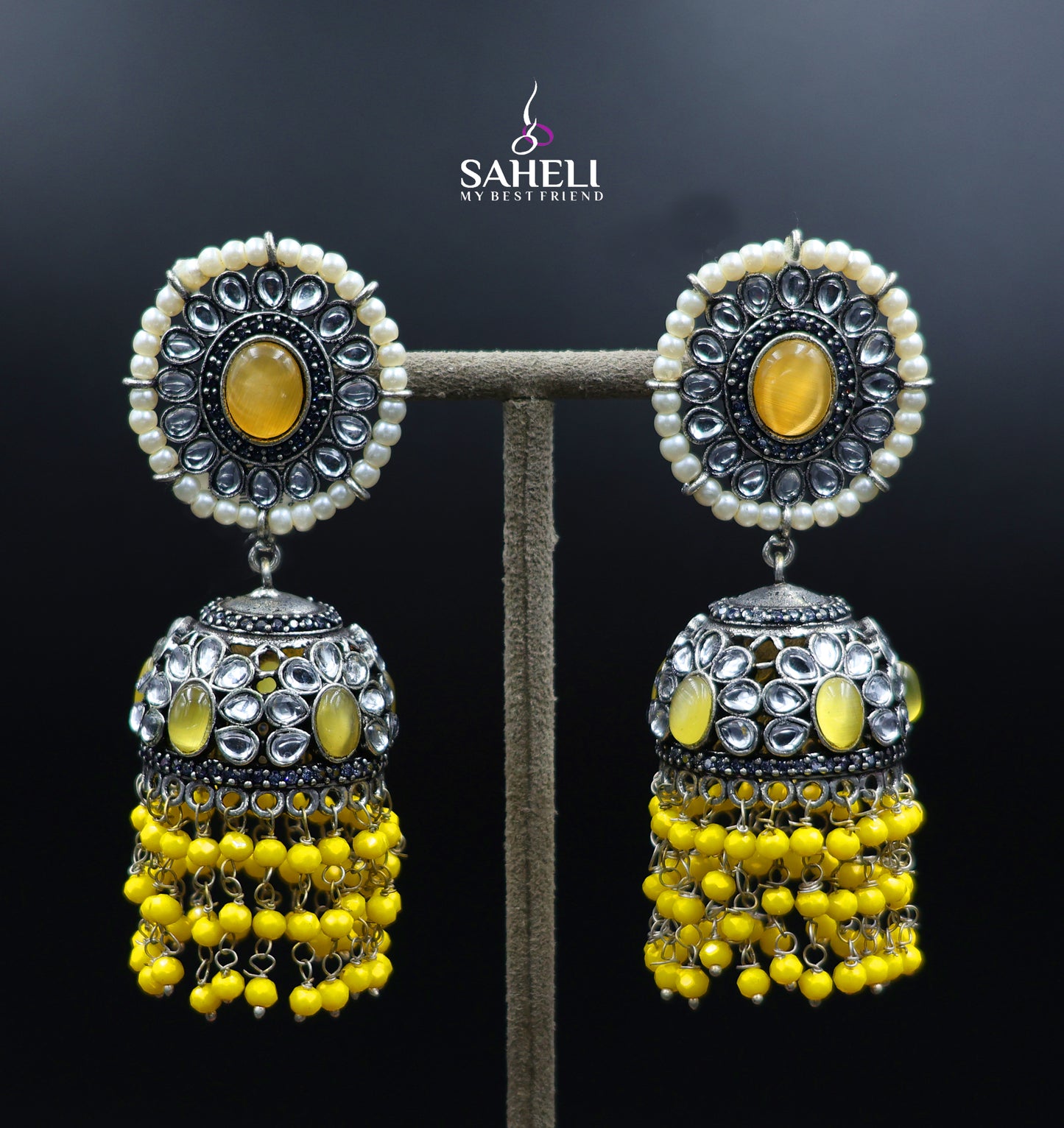 Yellow and silver earrings on a dark background with 'SAHELI' branding.