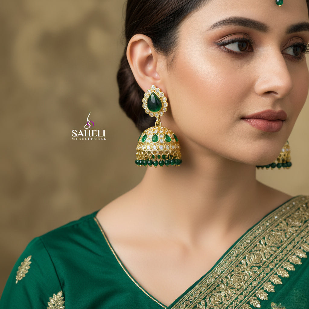 Gold and green gemstone earrings with 'Saheli' branding on a dark background