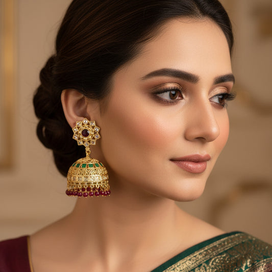 Ornate gold earrings with gemstones on a dark background, featuring the brand 'Saheli'.
