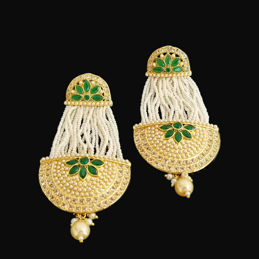 Pair of gold and white earrings with green gemstones on a dark background