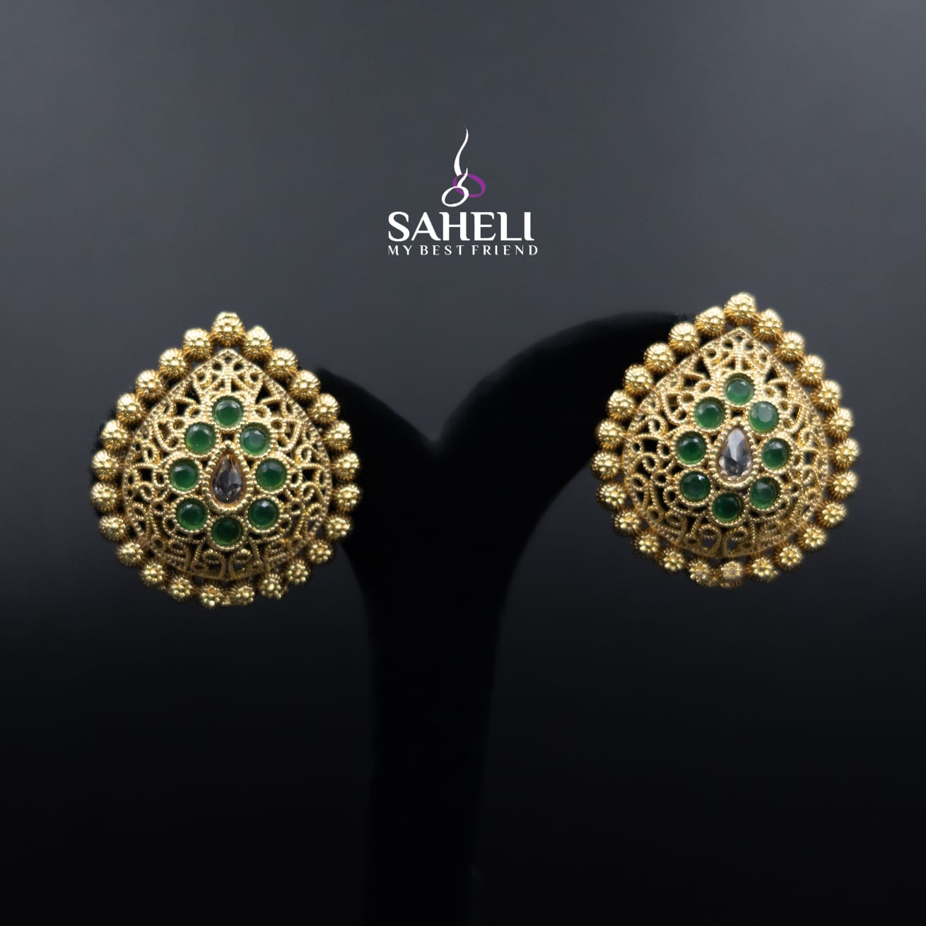 Gold earrings with green gemstones on a black background, featuring the brand 'Saheli'.
