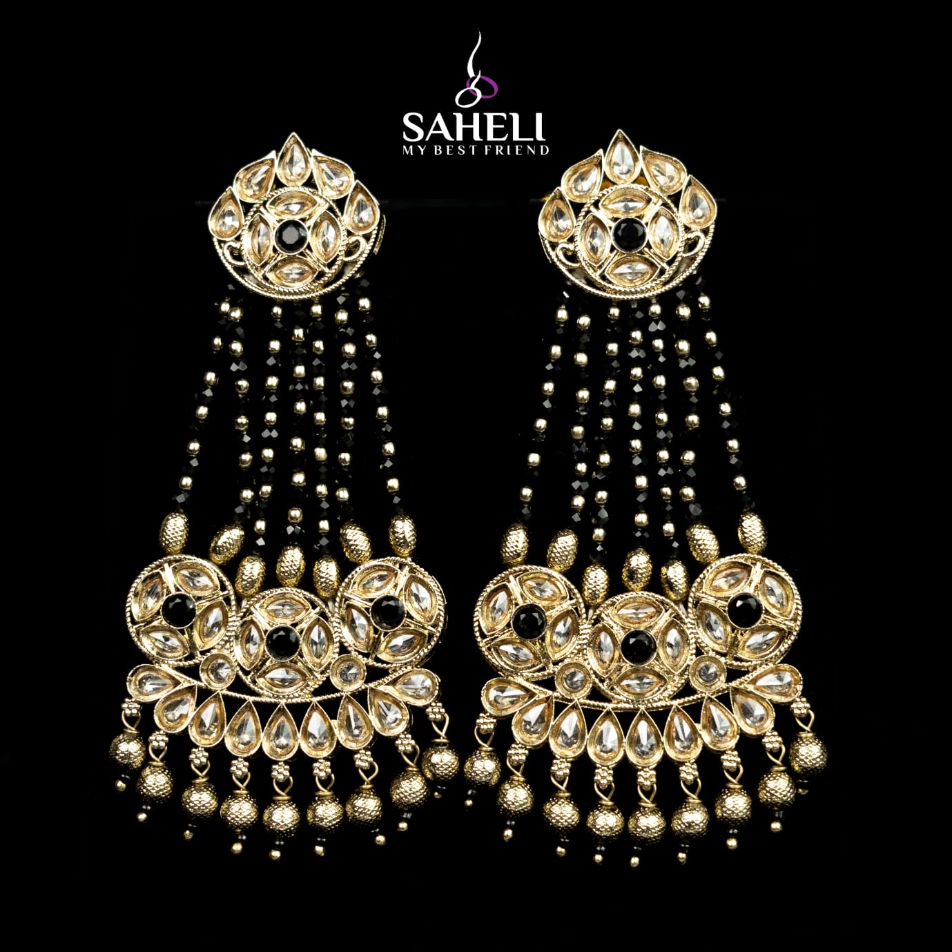 Ornate gold earrings with black stones on a black background, featuring the brand 'Saheli'.