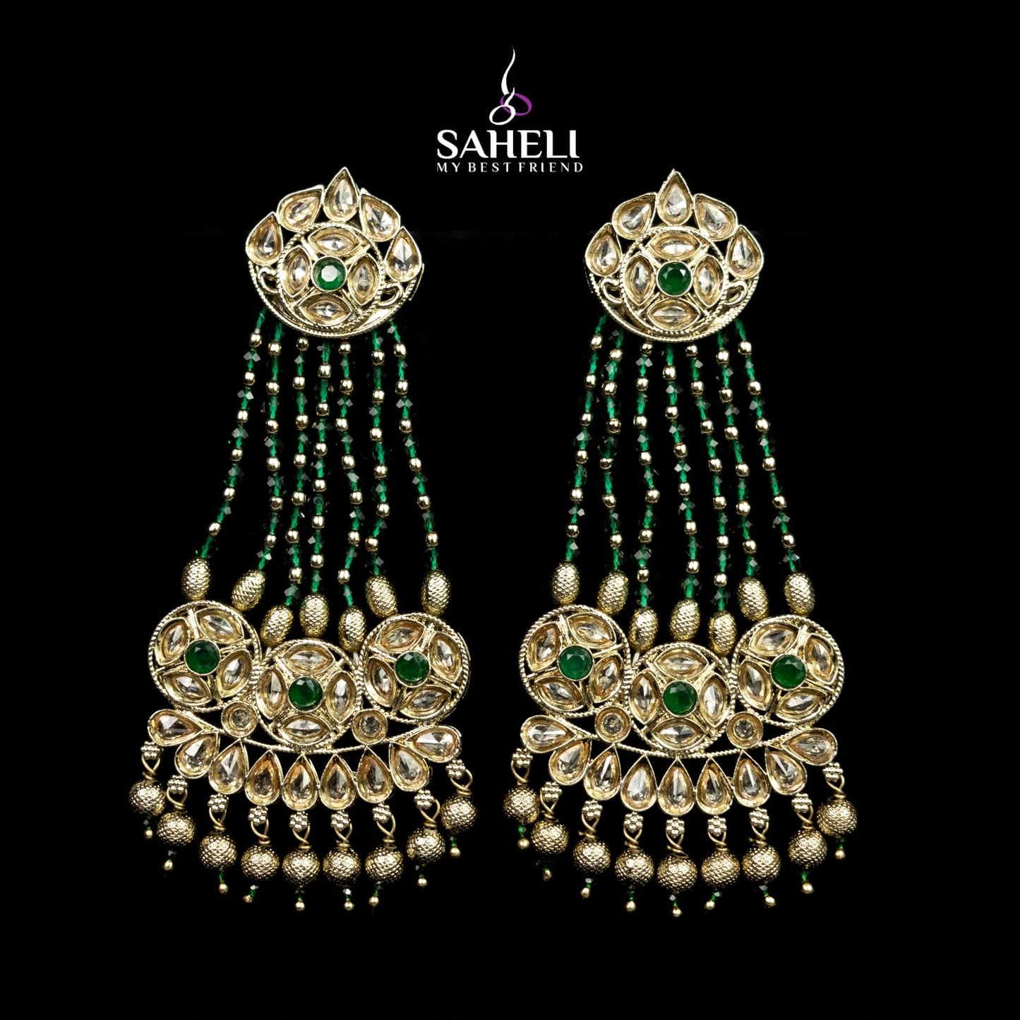 Ornate earrings with green stones on a black background, featuring the brand 'Saheli'.
