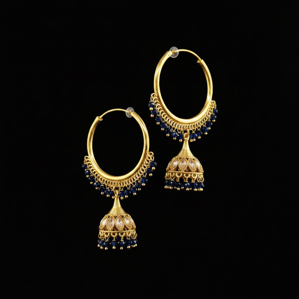 A pair of gold-toned traditional hoop earrings with dangling jhumka-style charms, decorated with small dark blue beads and clear stones, displayed on a gray jewelry stand against a light gray background.