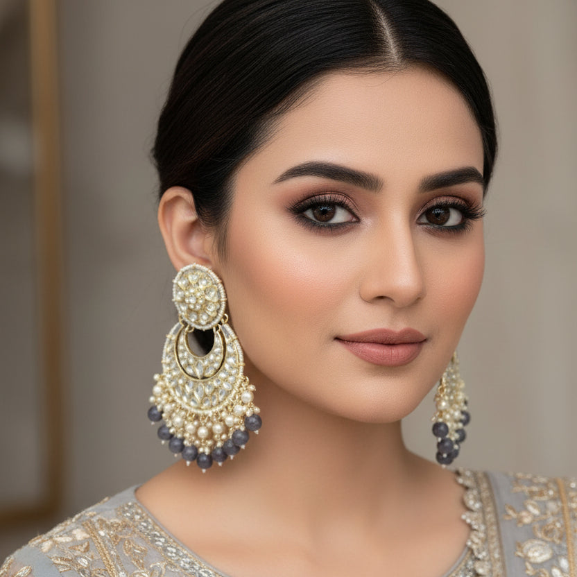 Pair of ornate earrings with gold, pearl, and dark beads on a black background