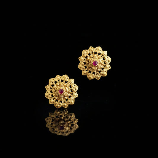 Pair of gold floral earrings with red gemstones on a gray background