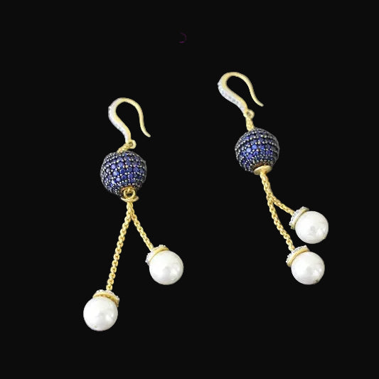 Pair of earrings with blue gemstones and white pearls on a gray background, branded 'SAHELI'.