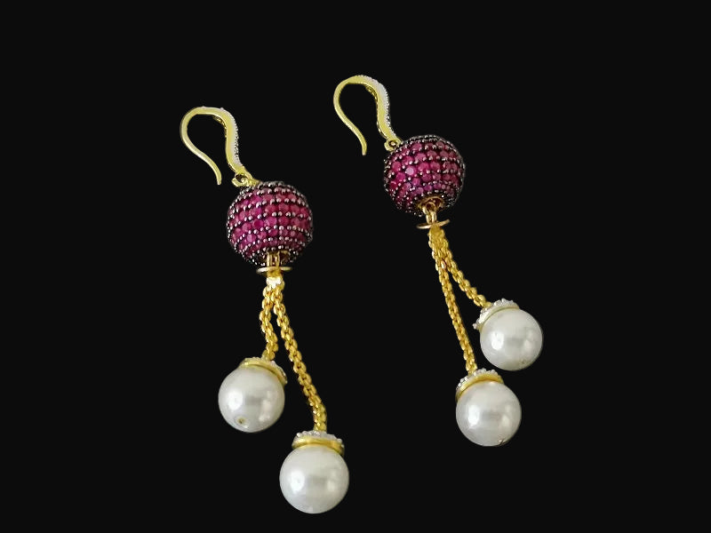 Pair of earrings with pink gemstones and pearl drops on a dark background, branded 'Saheli'.