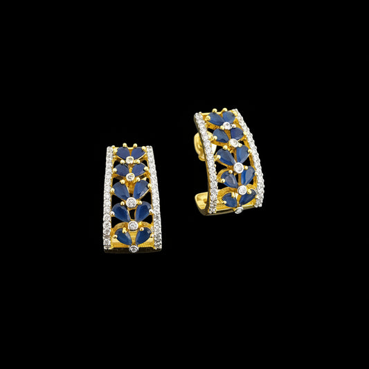 Pair of gold and blue earrings on a gray background with 'Saheli' branding.