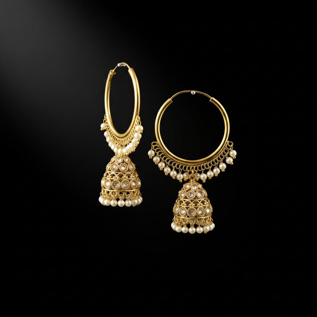 A pair of gold-toned traditional hoop earrings with dangling bell-shaped jhumka motifs, decorated with small white pearls and set with clear stones, displayed against a solid black background.
