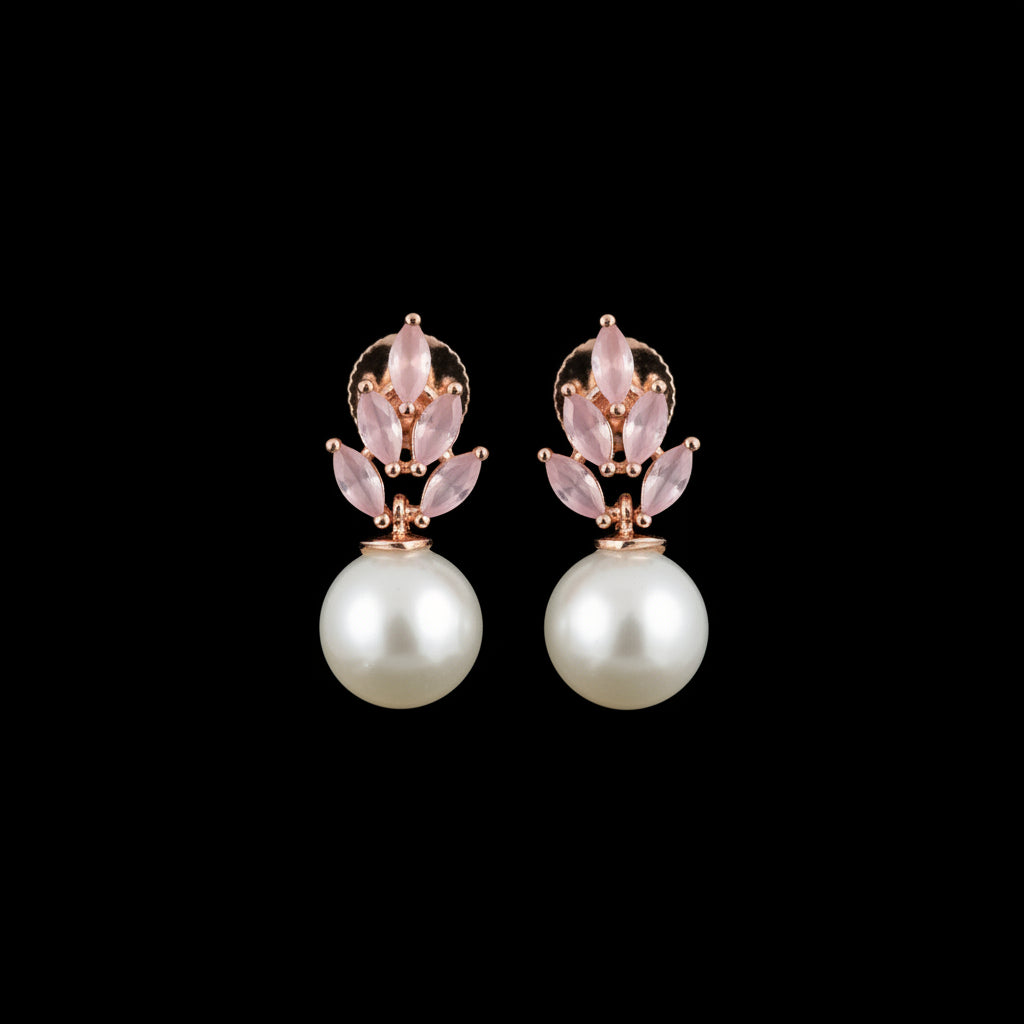 A pair of rose gold floral stud earrings with pale pink stones and a white pearl drop, displayed on a black textured stand against a dark gray background.