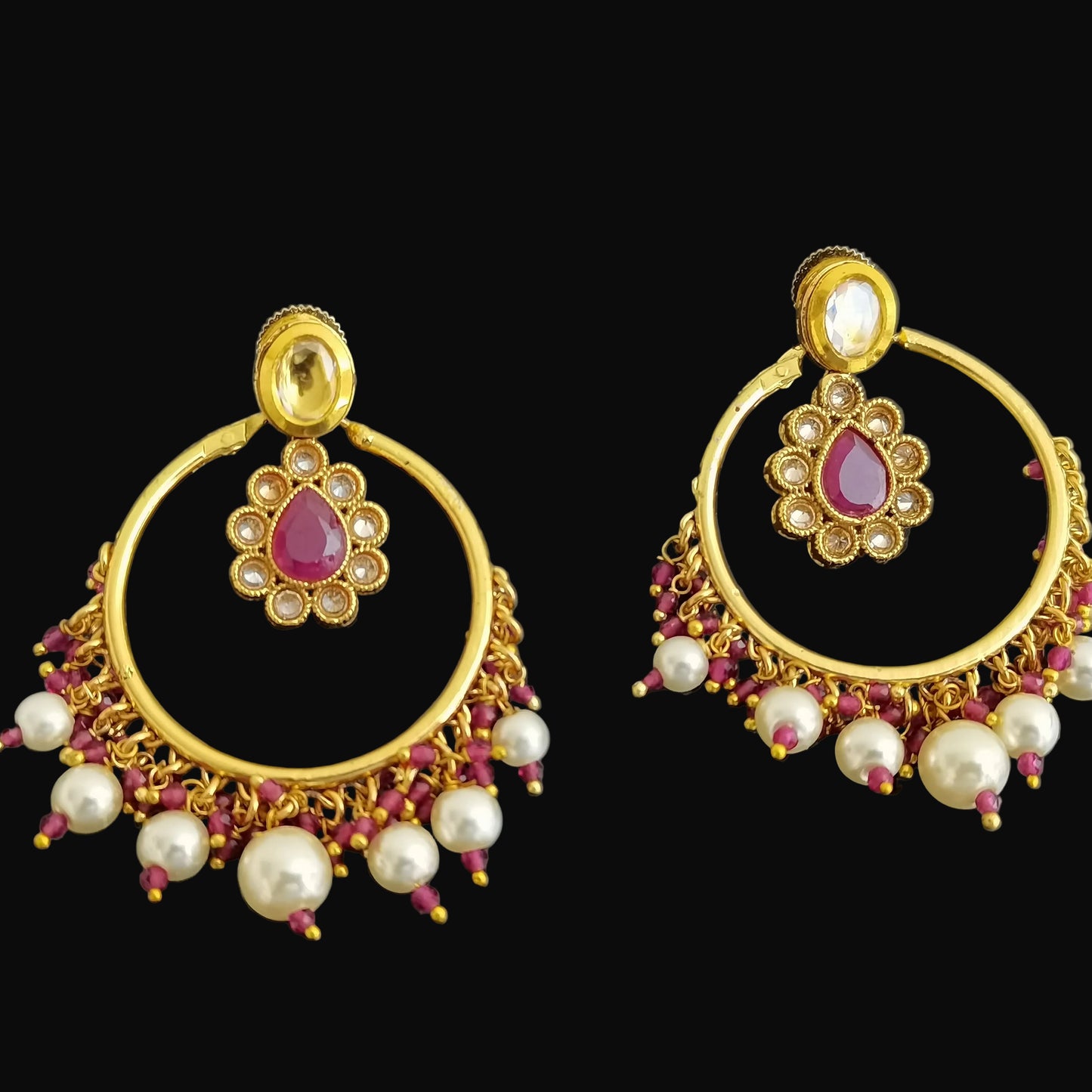 Gold earrings with pearls and red stones on a black background