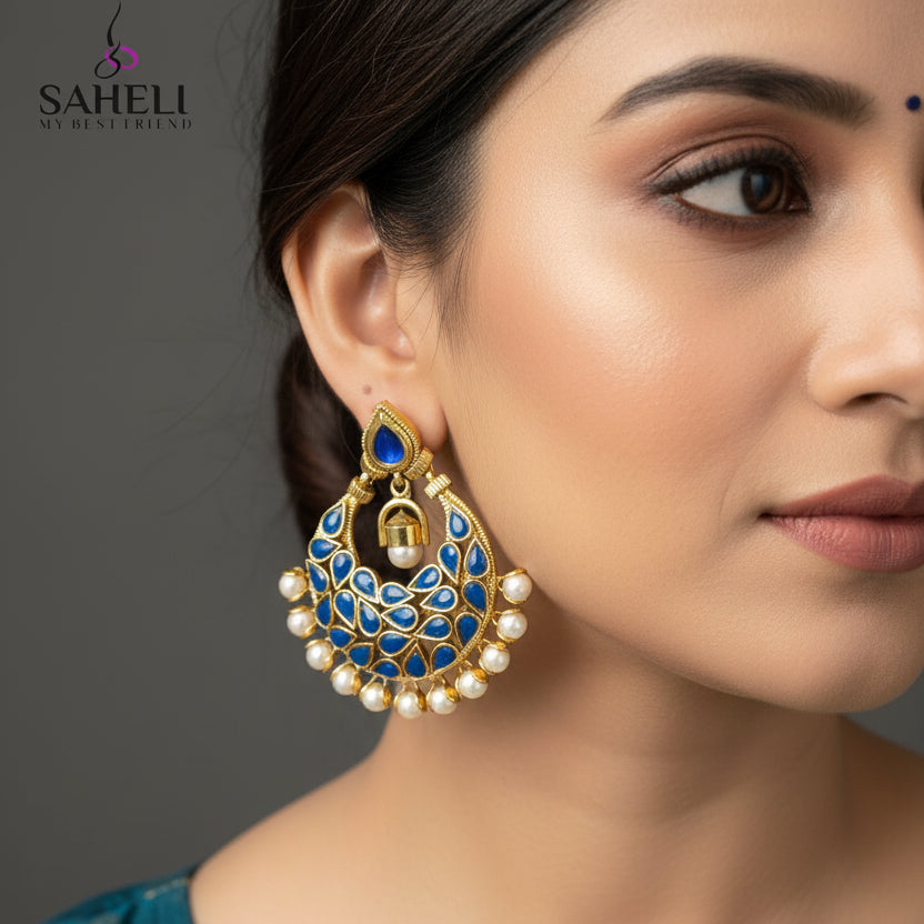 Pair of gold and blue earrings with pearls on a dark background, featuring the brand 'Saheili'.