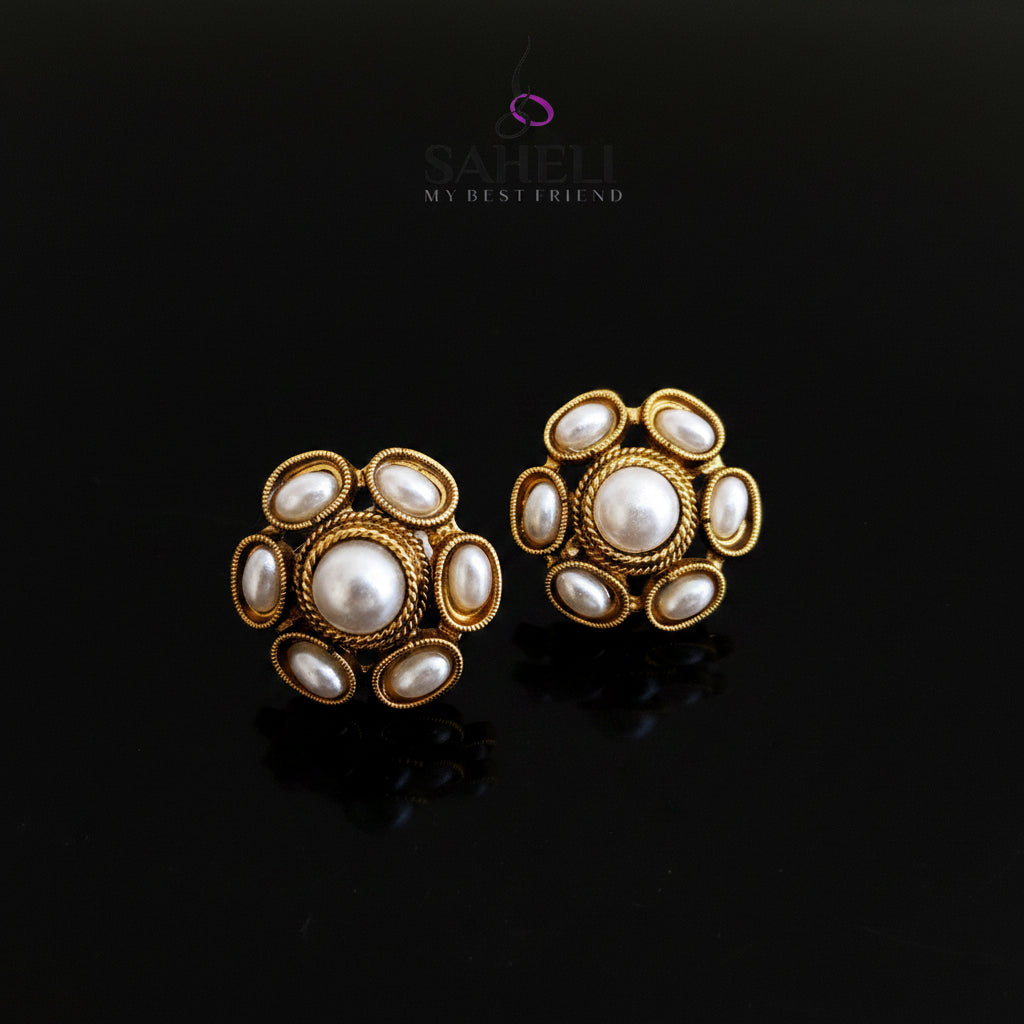 Gold and pearl earrings on a gray background with 'Saheli' branding.