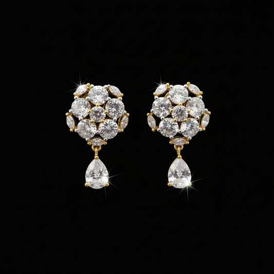 A pair of gold-toned statement earrings with clear gemstones, displayed on a black stand against a gray background with the brand name 'SAHELI MY BEST FRIEND' at the top.