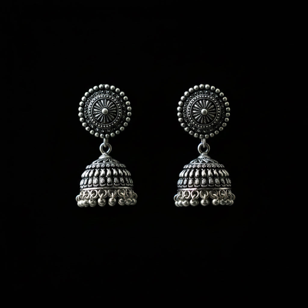 Silver jhumka earrings on a peacock feather with a dark background
