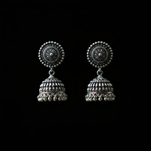 Silver jhumka earrings on a peacock feather with a dark background