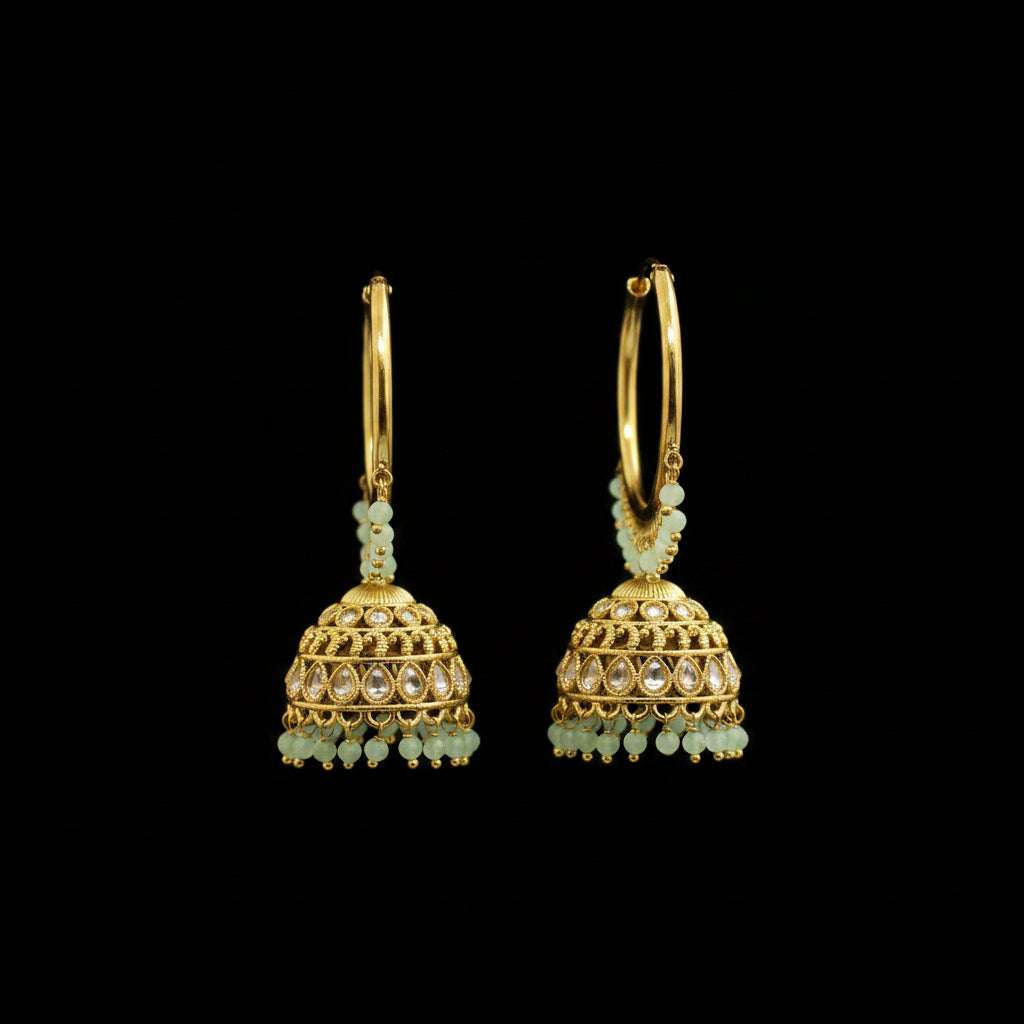 Gold hoop earrings with green beads on black earring stands against a gray background