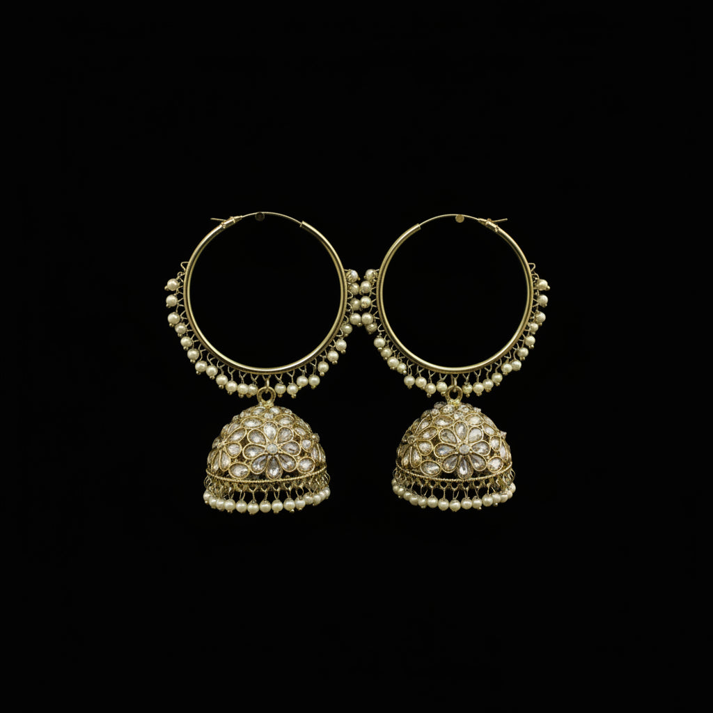 A pair of gold-toned Indian jhumka earrings with white pearl bead borders and dangling ornate filigree bells, displayed on black stand forms against a dark gray background.