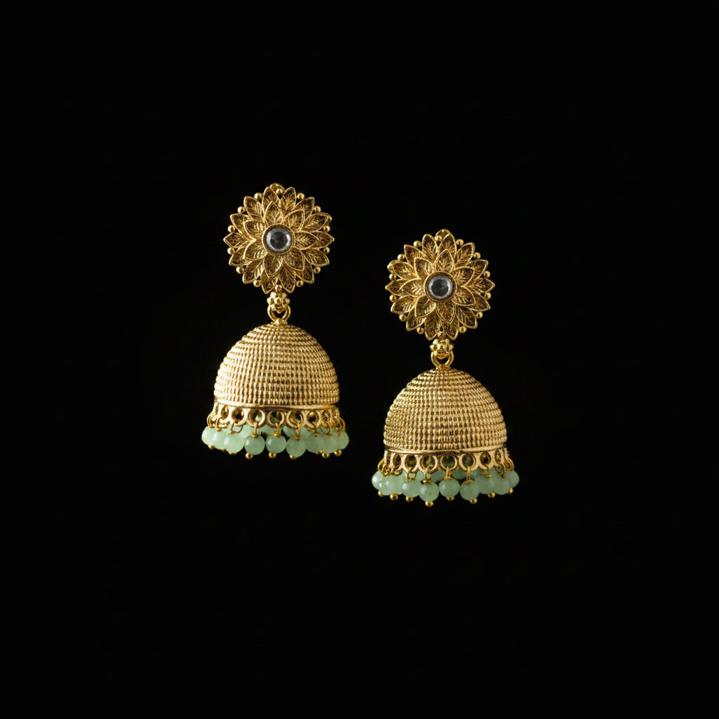 Gold and green earrings on a gray stand with a blurred background