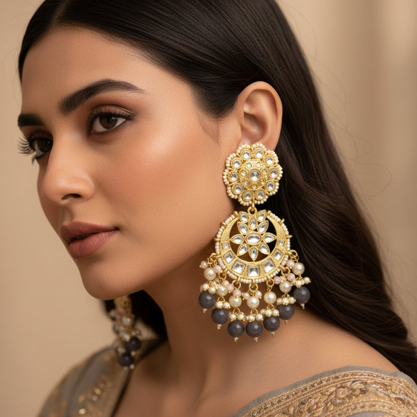 Pair of ornate earrings with gold, pearls, and beads on a dark background