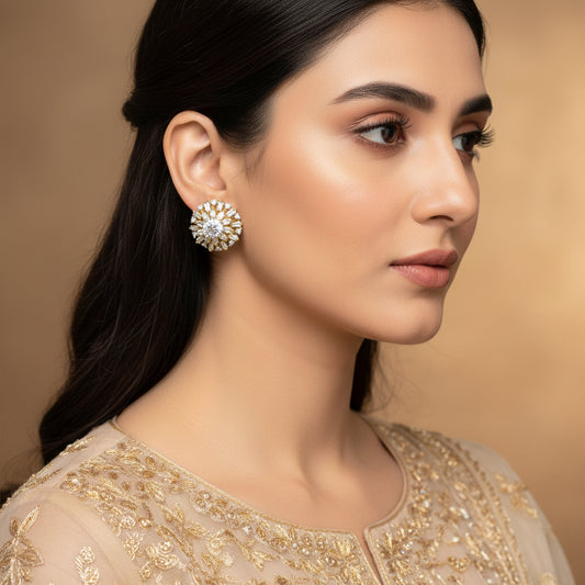 Pair of gold and diamond earrings on a dark background with 'Saheli' branding.