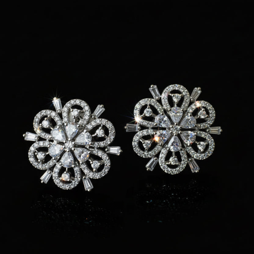 Pair of silver floral earrings on a black background with 'SAHELI' branding.