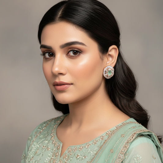 Pair of earrings with green gemstones and diamond-like stones on a dark background, branded 'Saheli'.
