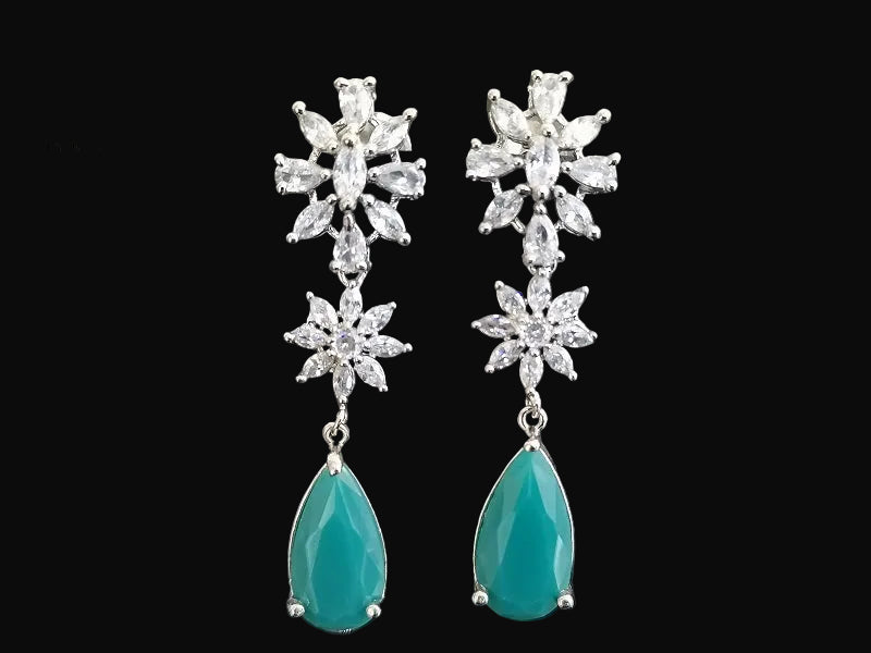 Pair of earrings with star-shaped top and teardrop-shaped bottom on a gray background, branded 'SAHELI'.