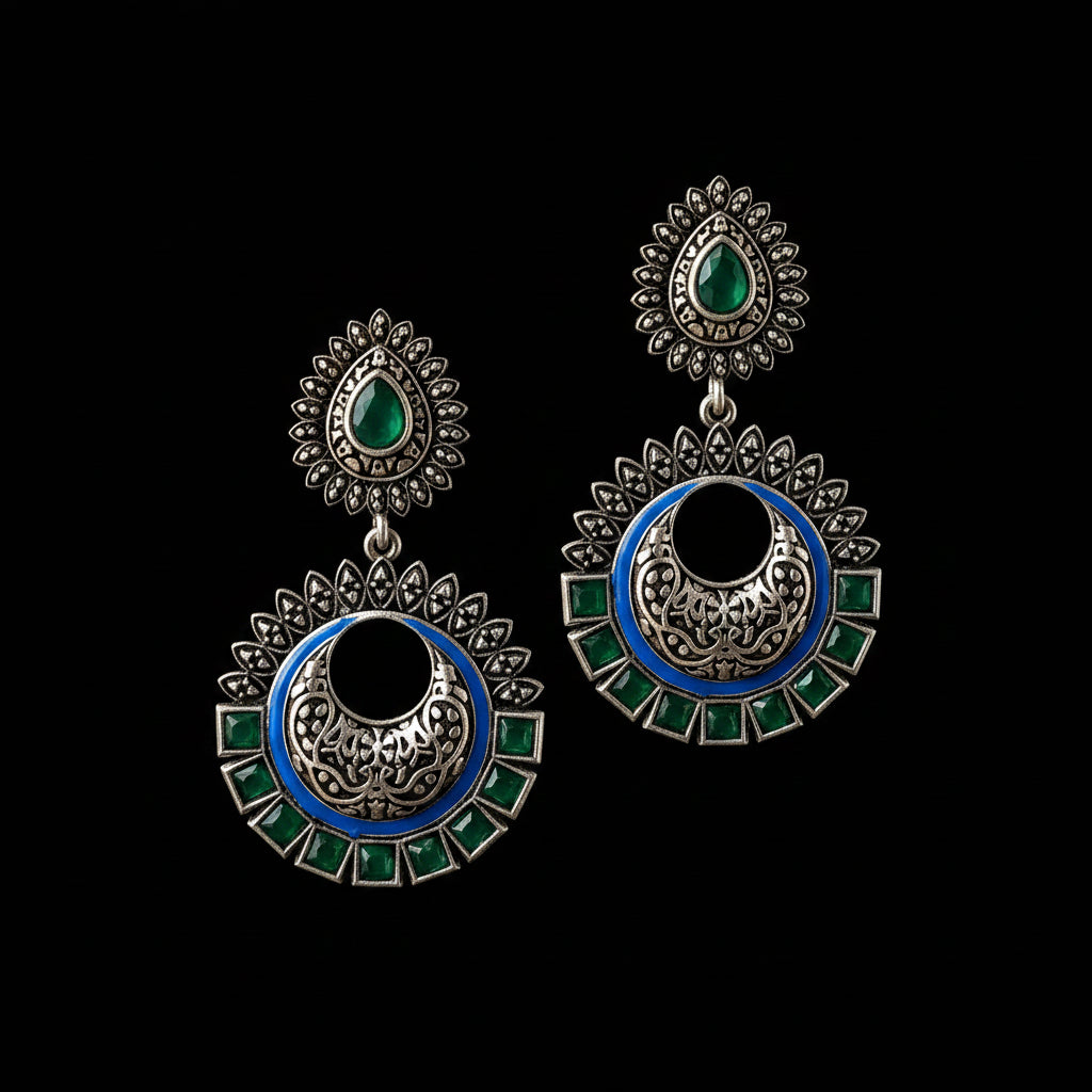 Ornate earrings with green and blue accents on a gray stand, branded 'Saheli'.