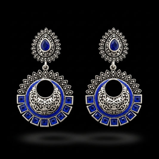 Ornate silver and blue earrings on a stand with 'SAHELI' branding.