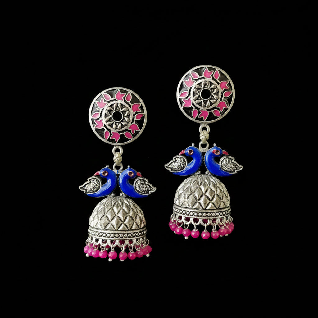 Ornate earrings with blue birds and pink beads on a gray stand against a black background