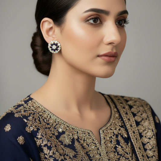 Pair of gold earrings with blue and white gemstones on a gray background, featuring the brand 'Saheli'.
