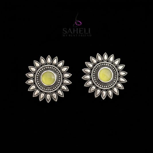 Silver sun-shaped earrings with yellow centers on a gray background, featuring the brand 'Saheli'.