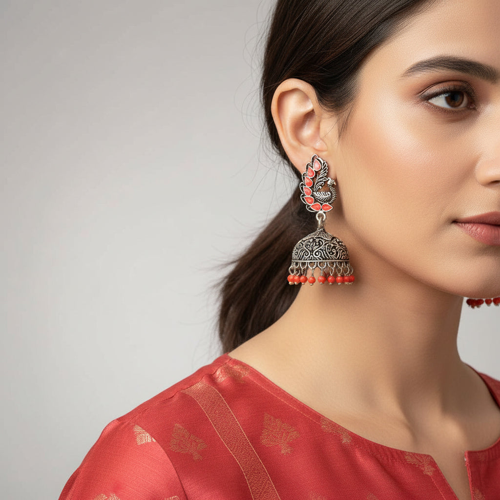 Ornate silver earrings with red beads on a gray stand, featuring the 'SAHELI' brand.