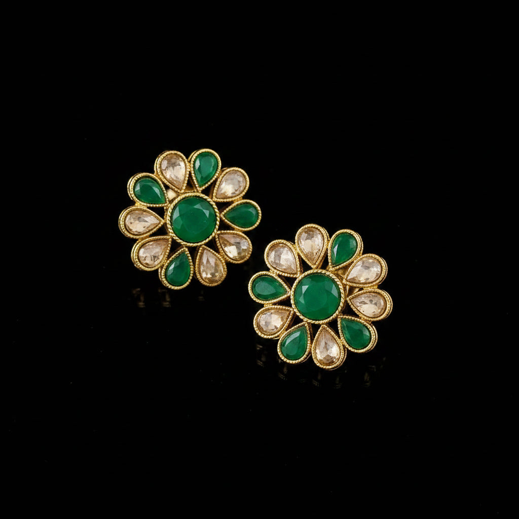 Floral earrings with green gemstones and gold accents on a gray background, featuring the brand 'Saheli'.