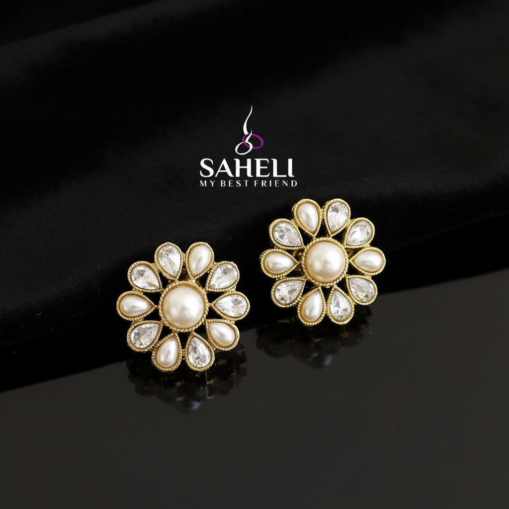 Pair of gold and pearl earrings on a dark background with 'SAHELI' branding.