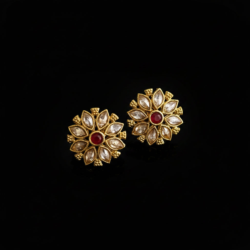 Gold floral earrings with red gemstones on a gray background, featuring the 'Saheli' brand.