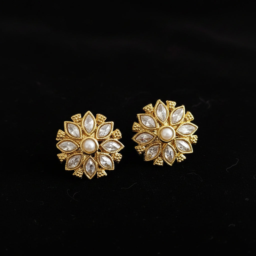 Gold floral earrings with white stones on a gray background, featuring the brand 'Saheli'.