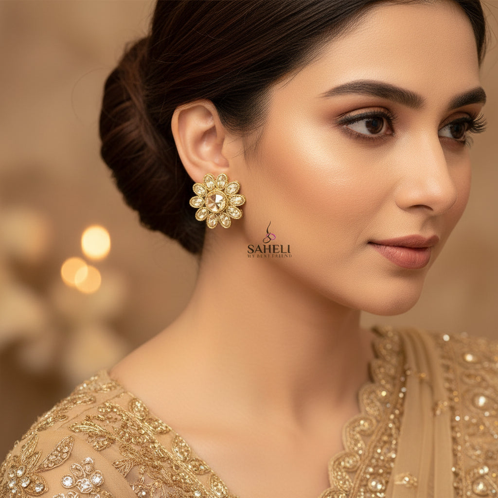 Gold floral earrings with clear stones on a gray background, featuring the brand 'Saheili'.